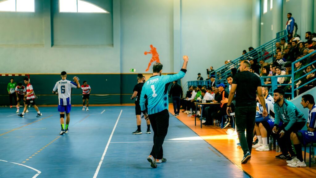 Dynamic handball match with players, referees, and spectators in a gymnasium.