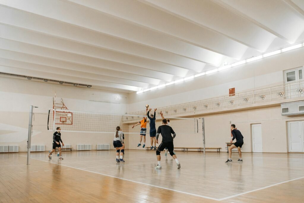 Indoor volleyball game with mixed gender players jumping to spike the ball.