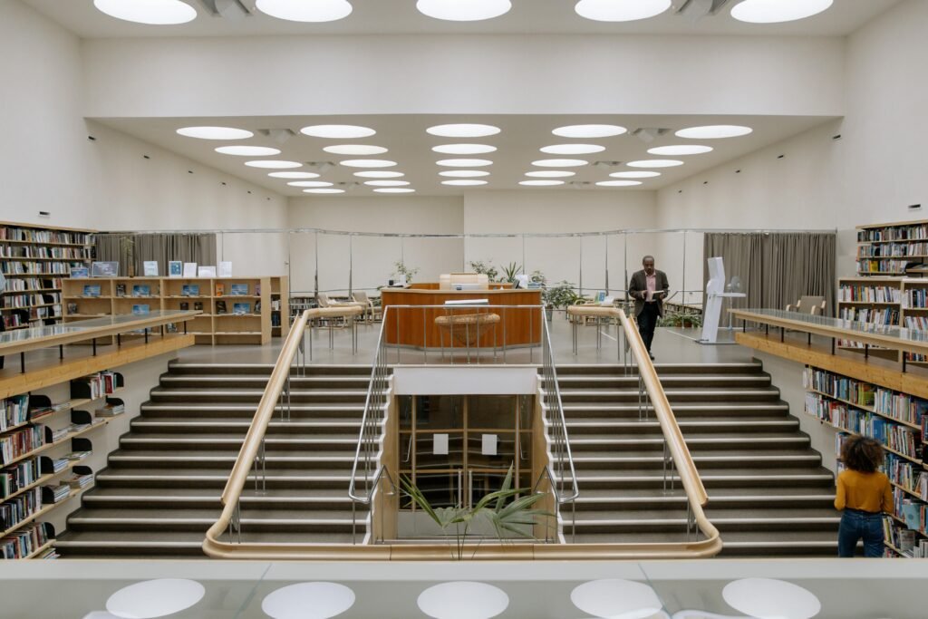 African American male and anonymous woman between bookcases with assorted literature in library with staircases