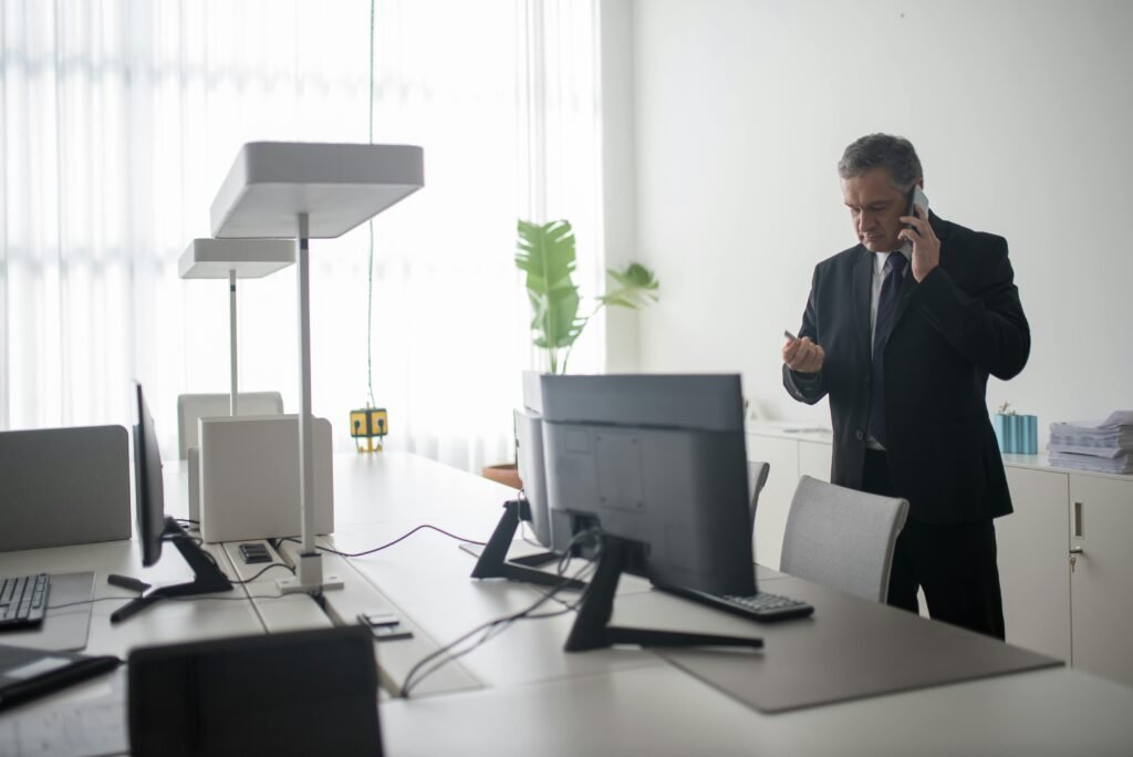 Un homme d’affaires senior en costume noir passe un appel dans un bureau moderne baigné de lumière.