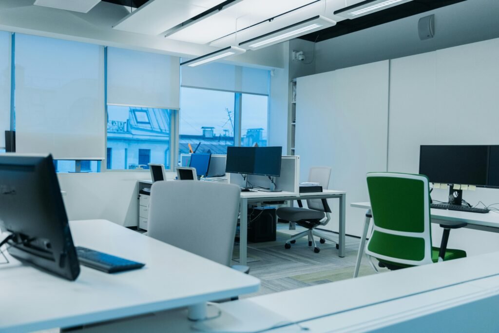 Environnement de bureau lumineux et moderne, doté de postes informatiques et de grandes fenêtres.